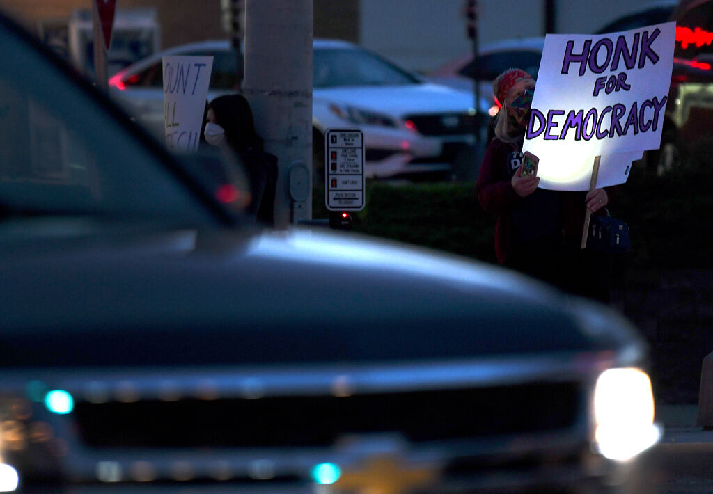 A protester holds a sign saying "Honk for Democracy" while cars go by on Wednesday at Providence Rd. and Broadway Blvd.